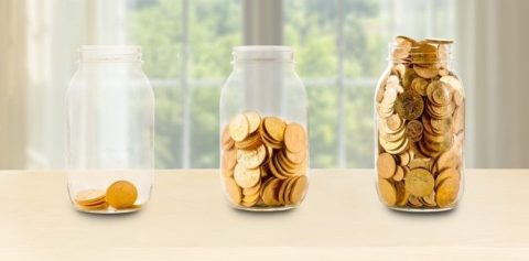 Drei mit Goldmünzen gefüllte Gläser in verschiedenen Höhen, die das Wachstum des Reichtums durch disziplinierte, kontinuierliche Investitionen symbolisieren.