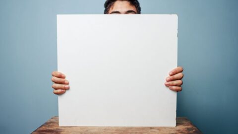 Eine Person hält ein leeres Whiteboard, das ihr Gesicht teilweise verdeckt, und ist bereit für eine Präsentation.