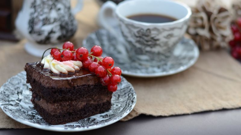 A chocolate cake garnished with red currants beside a cup of coffee, symbolising the seamless partnership between custodian banks and wealth managers.