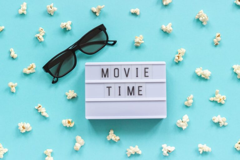 Ein Leuchtkasten-Schild mit „Movie Time“, Popcorn und Sonnenbrille auf türkisfarbenem Hintergrund, perfekt für einen Blog über Investmentbanking-Filme.