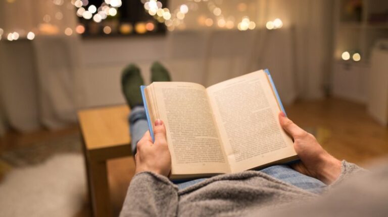 Eine Person liest ein Buch, während sie sich in der Neujahrswoche in einem Haus mit warmem Licht im Hintergrund entspannt. Hier finden Sie Finanzlektüre für Vermögensverwalter und Privatbankiers.
