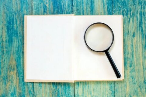 Ein Vergrößerungsglas auf einem aufgeschlagenen Buch, das die Suche nach der besten Depotbank für unabhängige Vermögensverwalter symbolisiert.