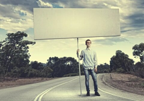 A person holding a large blank signboard on an empty road, representing opportunities and strategies in wealth management advertising.