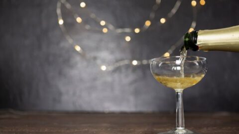 Champagner, der in ein Glas gegossen wird, mit festlichen Lichtern im Hintergrund, die Feierlichkeiten und Erfolge symbolisieren. Ein Jahr voller Herausforderungen