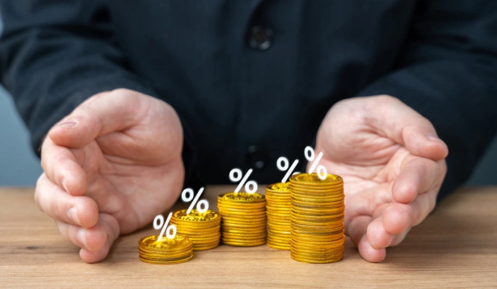 Hands shielding stacked gold coins with percentage symbols, illustrating compound interest accumulation