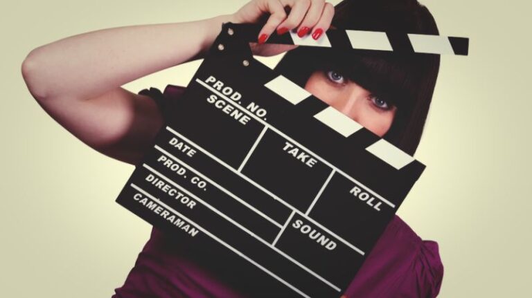 A woman in a purple dress holding a film clapperboard, symbolising celebrity financial planning and wealth management strategies.