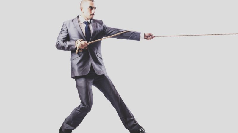 A determined businessman in a suit pulling a rope, symbolising the competitive tension between traditional banks and independent external asset managers (EAMs) in the wealth management sector.