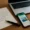 Ein handgeschriebener Urlaubsbrief, ein Smartphone mit einer WhatsApp-Nachricht aus Mallorca und ein Laptop auf einem Holztisch symbolisieren den Kontrast zwischen traditionellen Briefen, digitaler Kommunikation und KI-Eingabeaufforderung in der Vermögensverwaltung.