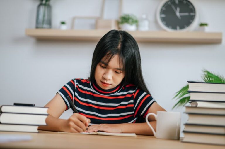 Woman writing at desk surrounded by books — symbolising complexity of KYC documentation