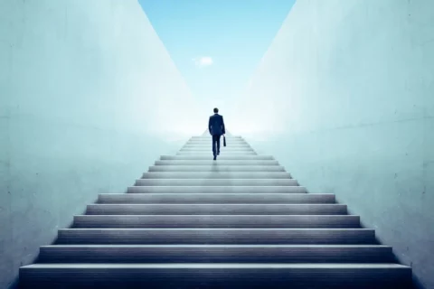 Ein Geschäftsmann, der eine lange Treppe hinaufgeht, symbolisiert den Zinseszinseffekt und das stetige finanzielle Wachstum im Laufe der Zeit.
